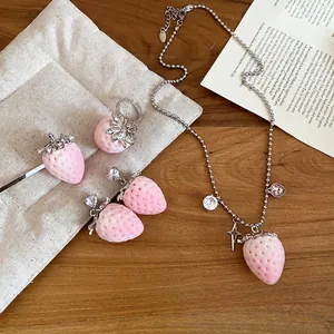 Pink strawberry jewelry set with necklace and earrings on a minimalist quilted pouch