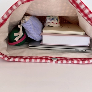 Interior detail of red checkered tote bag showing laptop and storage space with magnetic clasp