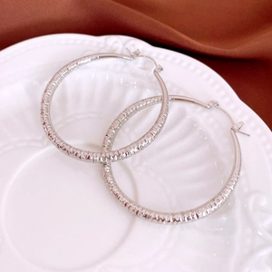 Detailed view of silver striped hoop earrings placed on an elegant white textured ceramic plate