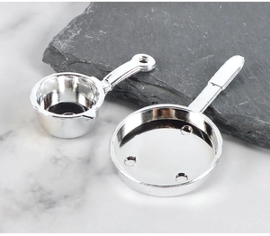 Miniature silver dollhouse pans with polished chrome finish on a stone surface