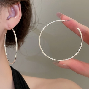 Close-up of stylish large silver geometric hoop earrings worn by a model to show size