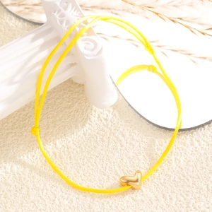 Vue macro du bracelet en corde tressée jaune réglable avec pendentif cœur doré poli