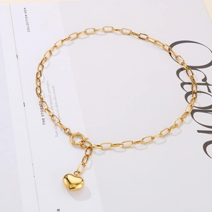 Detailed view of a gold-toned square link chain necklace with a 3D heart pendant on a book