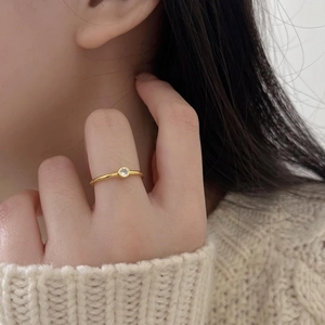 Close-up of a delicate gold silver ring with a single sparkling zircon on a model finger