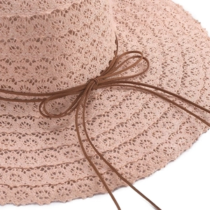 Detail of light pink lace straw hat with intricate woven texture and brown bow ribbon