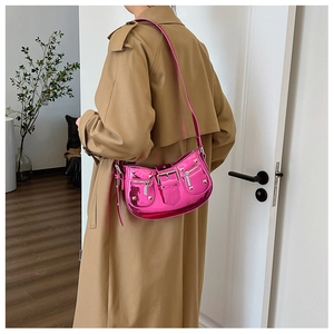 Hot pink patent leather shoulder bag with rivets and buckles shown on a model's arm
