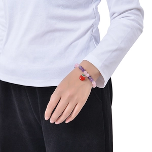 Bracelet perlé rose et violet avec un charm pomme rouge porté au poignet d'un modèle