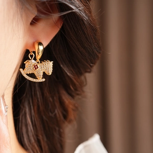 Close-up of gold rocking horse earring with tiny crystals and a red gemstone on model