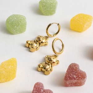 Close-up of golden stainless steel teddy bear drop earrings on white background with candies