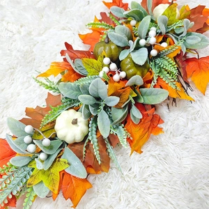 Close-up of autumn harvest wreath with orange pumpkins and maple leaves on white plush