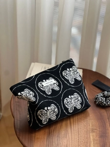 Gros plan sur la trousse de maquillage en toile noire avec broderie papillon blanche