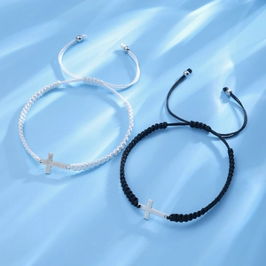 Detail view of woven black and white bracelets with adjustable metal cross pendants