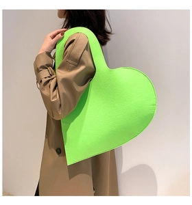 Close-up of oversized neon green felt heart-shaped tote bag shown on a fashion model