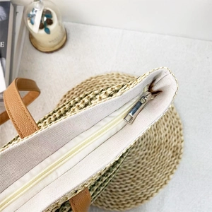 Detail of raffia woven bag showing green texture, leather handle and zipper closure
