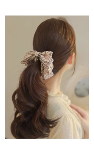 Detail of a beige bow hair clip with brown floral patterns on a model ponytail