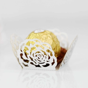 Detail of white laser-cut rose lace paper wrap with golden chocolate on mirror surface