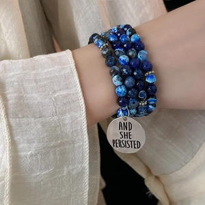 Detail of layered blue beaded bracelet with engraved round charm on person's wrist