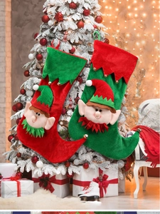 Detailed plush Christmas elf stockings in red and green hanging on a snowy Christmas tree