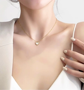 Detail of a gold heart pendant necklace with white shell inlay worn by a female model