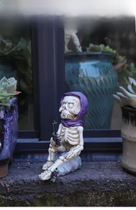 Macro detail of skeleton figurine with purple hood fishing next to succulent plants