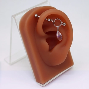 Detail eines Industrial-Piercing-Stabs mit Herzverbindung und buntem Tropfenanhänger