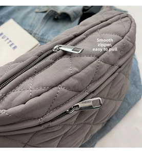 Detail view of smooth silver double metal zippers on grey quilted crossbody chest bag