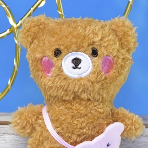 Close-up detail of a 12cm brown plush bear toy with a pink cross-body bag