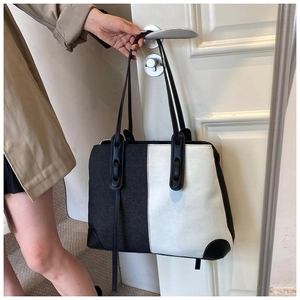Handheld display of a large black and white patchwork tote bag with leather handles