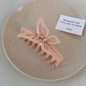 Close-up of a large beige butterfly-shaped hair claw clip on a ceramic decorative plate