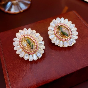 Macro detail of floral crystal stud earrings with pink zircon and green accents on leather