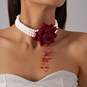 Détail d'une rose en tissu rouge foncé et d'un collier de perles multicouche avec glands