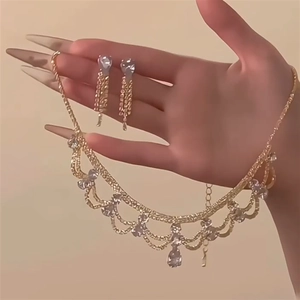 Elegant gold-tone jewelry set with teardrop crystals worn by a model in a natural setting
