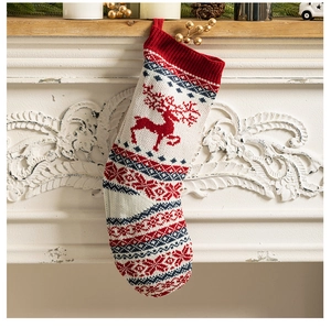 Knitted Christmas stocking with reindeer patterns hanging on a decorated white fireplace
