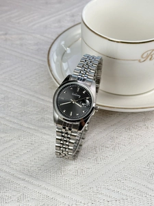 Detail of silver steel watch band with black dial featuring calendar window and markers