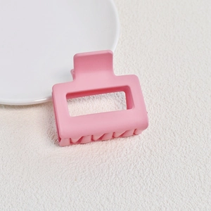 Close-up of matte pink rectangular hollow hair claw clip on white fabric surface