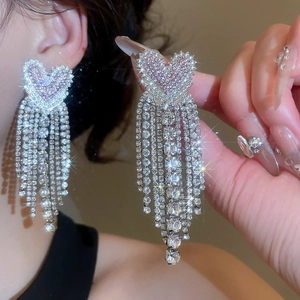 Close-up of sparkling heart tassel earrings with pink and white rhinestones on model