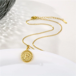 Macro shot of gold circular pendant with embossed letter P and beaded edge on a white tray