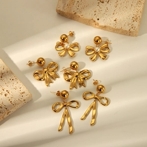 Detailed set of three golden bow earrings with pearls and long tassels on stone surface