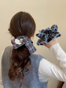 Close-up of retro plaid bow scrunchie set with white label in model's wavy brown hair