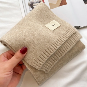 Close-up of beige knit scarf with 'emo' tag on soft fabric and ribbed edge details
