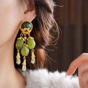 Close-up of vintage gold tassel earring with olive green gems on a model