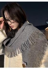Detail of grey knitted scarf with tassels shown on model against city night background