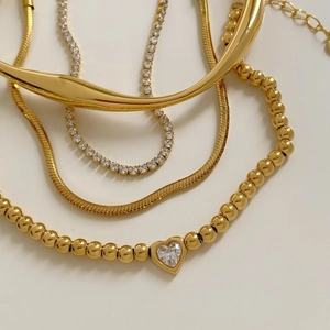 Dettaglio del set collana con ciondolo a cuore perlato e catena tennis in oro impilati