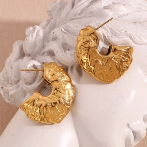 Macro view of 18K gold-plated earrings with hammered texture on a classic white sculpture