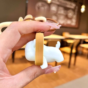 Side view of white cartoon dog silicone keychain with brown ring held by hand