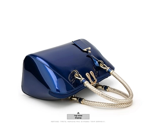Detail view of navy patent leather handbag with golden zippers and woven handles