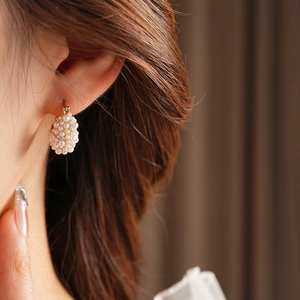 Close-up of elegant gold drop earrings with white pearls and small diamonds on a model