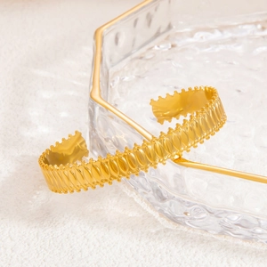 Detail of gold roman style open cuff bracelet with wavy texture on a glass tray