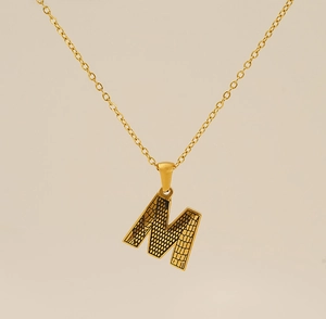 Détail d'un pendentif lettre M doré avec incrustation de texture crocodile noire