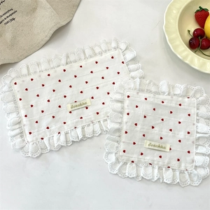 Close-up of white lace placemats featuring red heart patterns and Szakka brand label